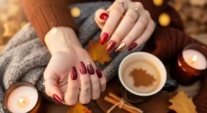 Flat-lay of hands showcasing five trendy red fall nails designs for 2025, including matte oxblood coffin nails, glossy cherry almond nails, , scarlet-to-burgundy ombré nails, and gold-leaf accented almond nails, styled with autumn leaves, knit scarf, latte, and candle in warm fall tones.”