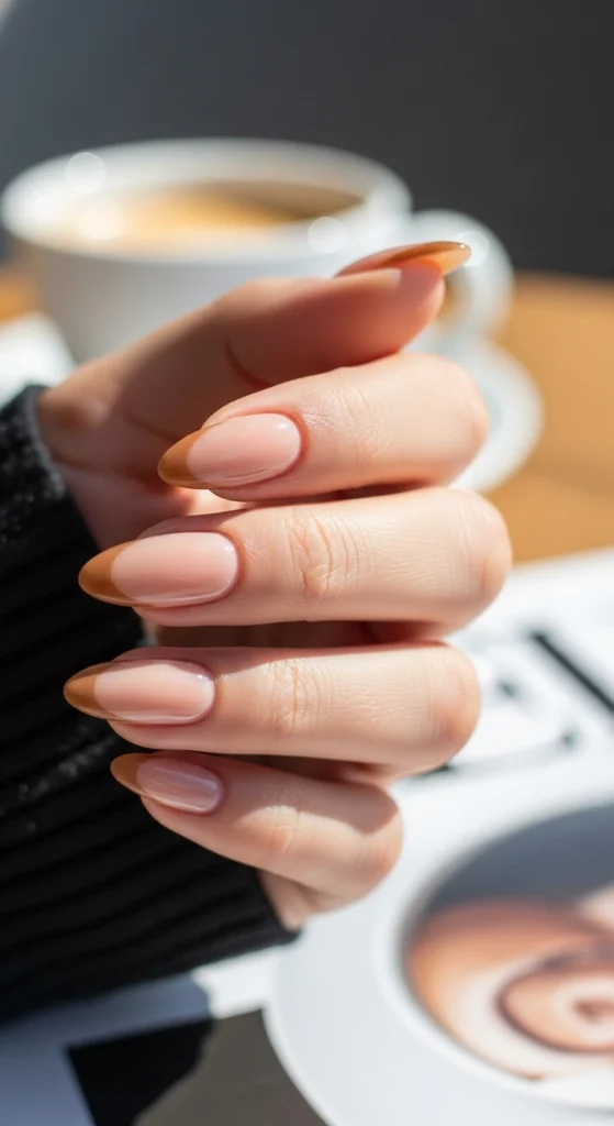 21 Fall Nails Inspiration 2026! Chic Trendy Autumn Manicures 17 Glossy nude almond nails with caramel brown French tips on a coffee table background, cozy casual mood.
