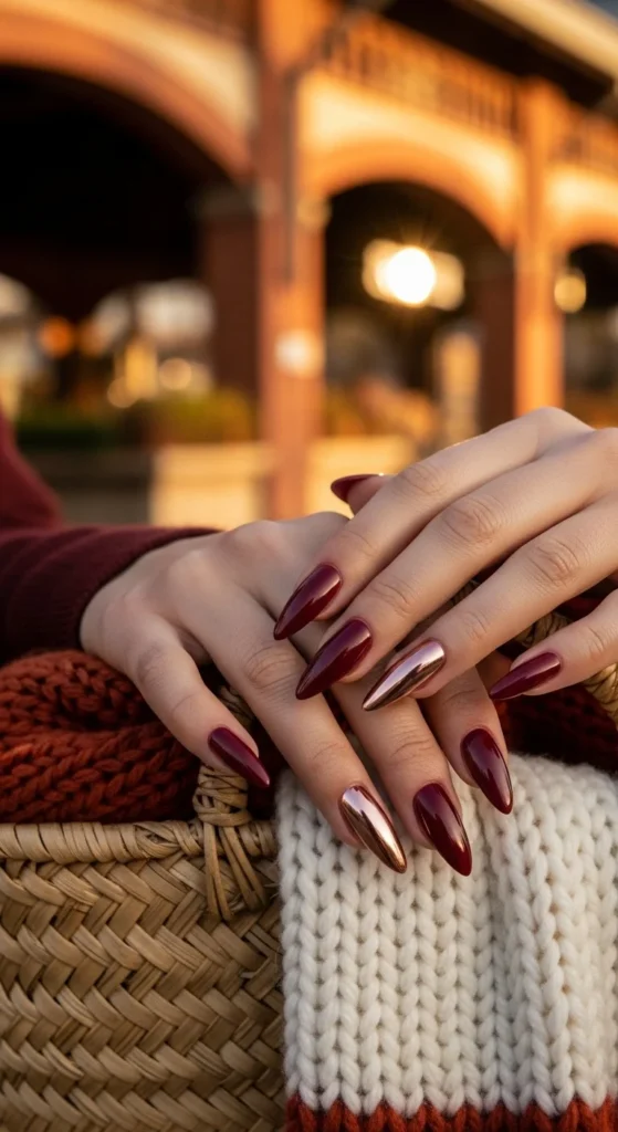 Editorial shot of cranberry stiletto nails with rose-gold chrome tips against autumn market.