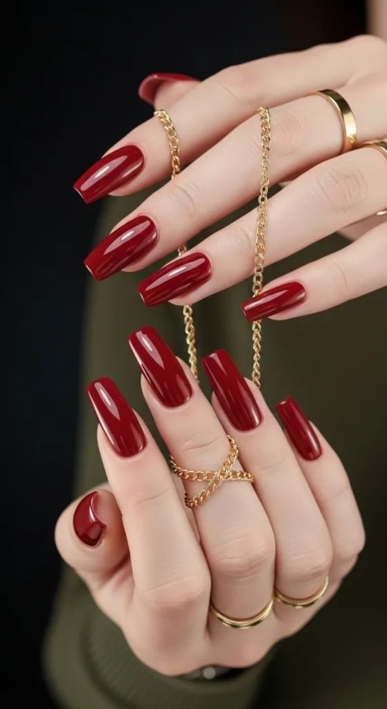 Glossy garnet long square nails holding chain in moody spotlight.