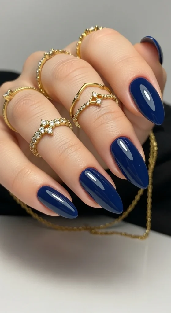Ink blue glossy almond nails with gold jewelry.