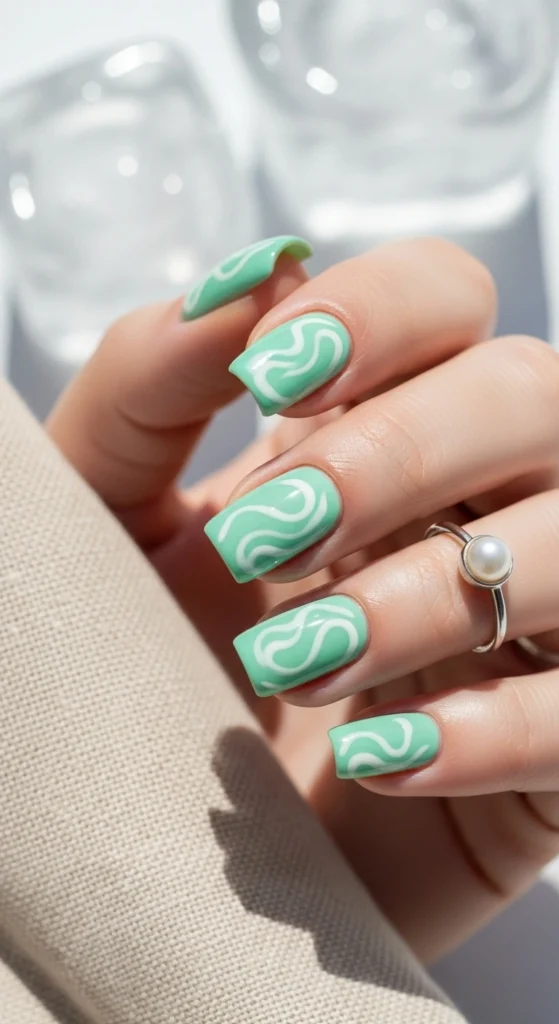 Close-up of square nails painted in mint green with glossy swirl accents.