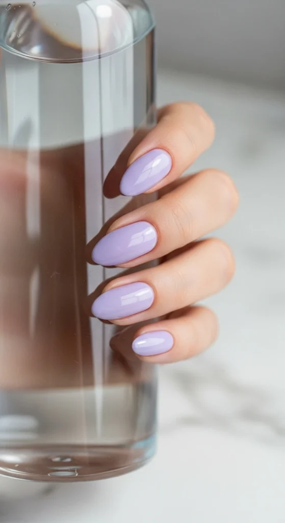 Soft lavender almond nails holding a water bottle on a marble background.