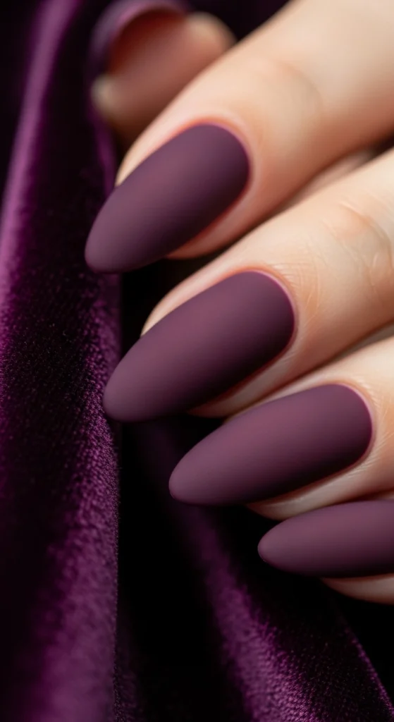 21 Fall Nails Inspiration 2026! Chic Trendy Autumn Manicures 18 Matte deep plum almond nails resting on dark velvet fabric, bold and luxurious appearance.