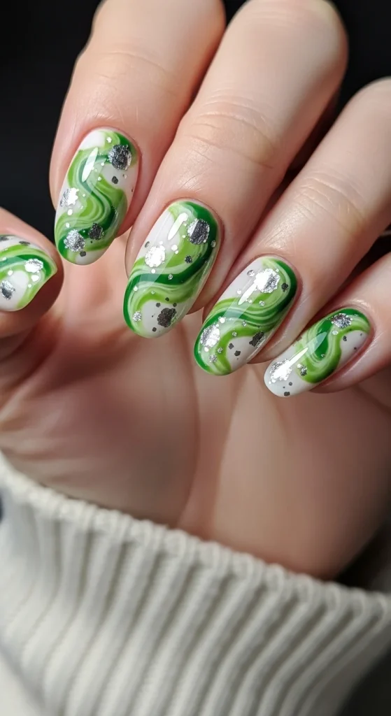 Short oval nails with matcha green swirls over pastel white, silver shimmer accents