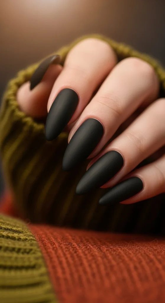 Black Fall Nails 2026: 19 Trendy Designs You’ll Love 2 Long almond nails painted matte black, styled with fall fashion accessories.