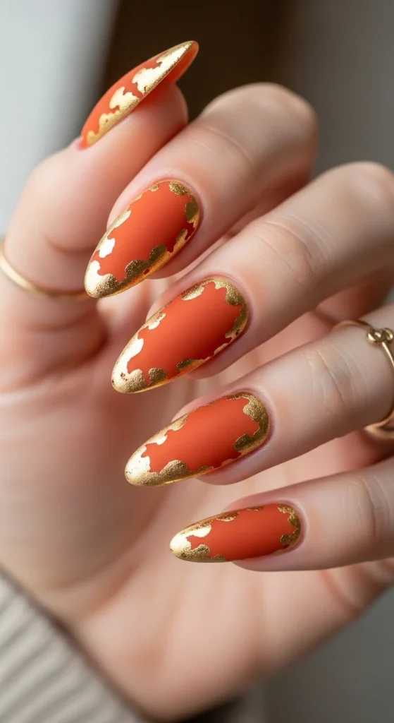 : Rust orange nails with irregular golden foil borders along edges
