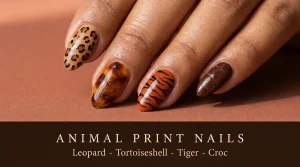 Close-up of four almond nails with leopard, tortoiseshell, tiger stripe and croc print designs on a dusty terracotta surface