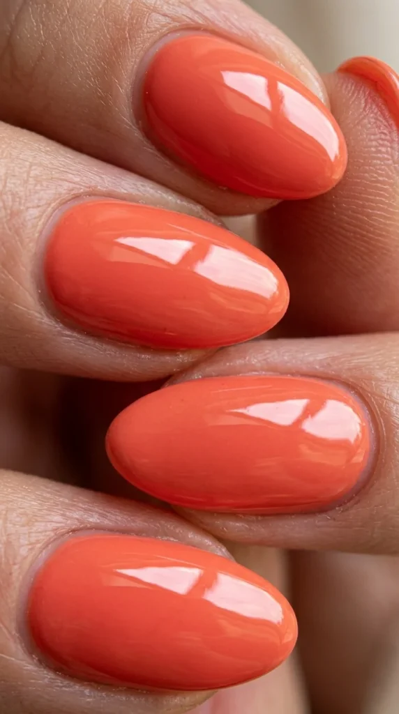 Macro close-up of glossy coral almond nails highlighting shine and manicure detail.