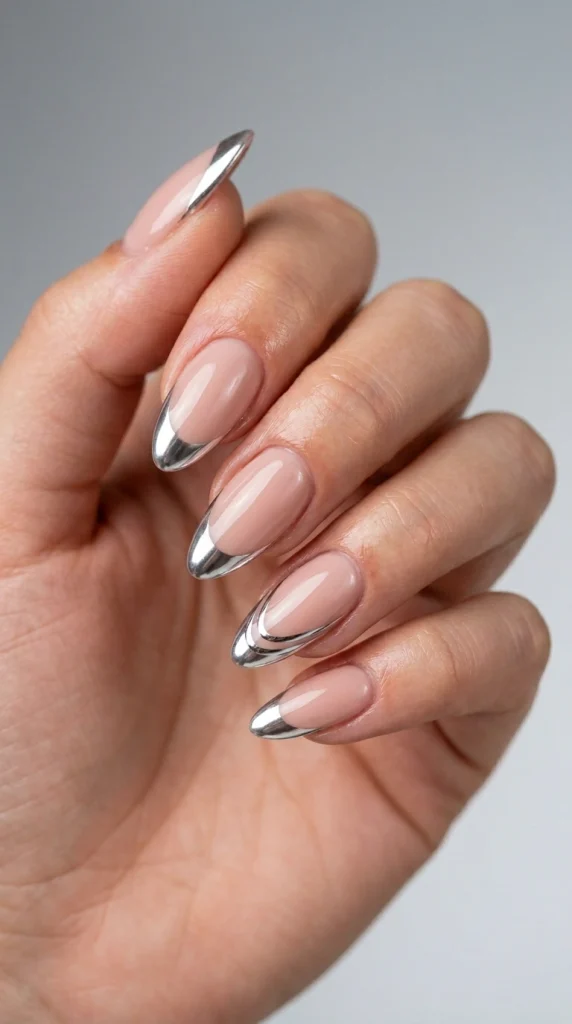 Close-up of nude almond nails with reflective chrome French tips.
