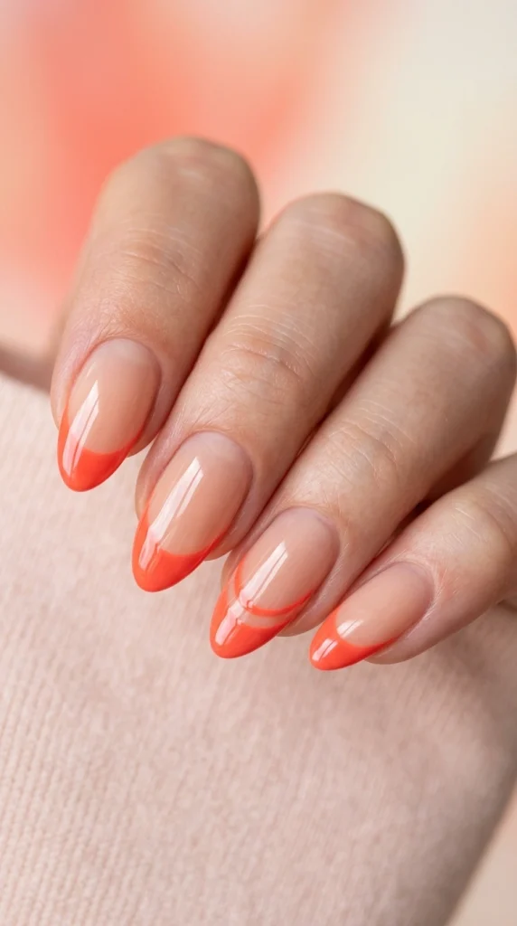 Close-up of sheer nude almond nails with bright coral French tips.
