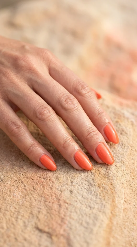 Close-up of glossy coral orange almond nails in a simple summer manicure.