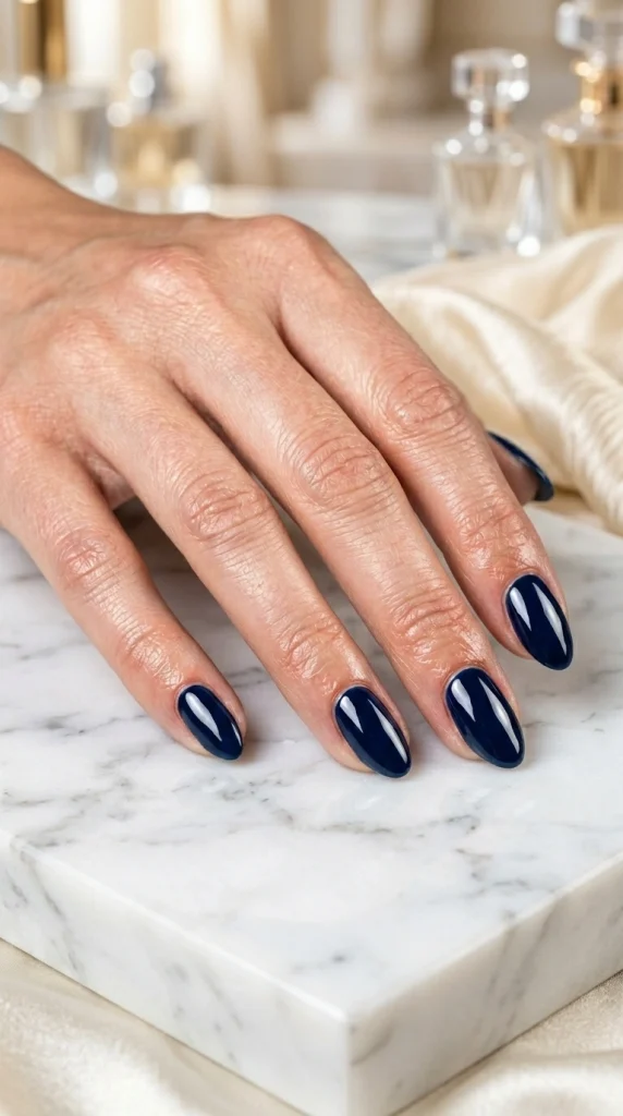 Close-up of glossy inky navy almond nails, a deep blue unexpected summer nail color for 2026.