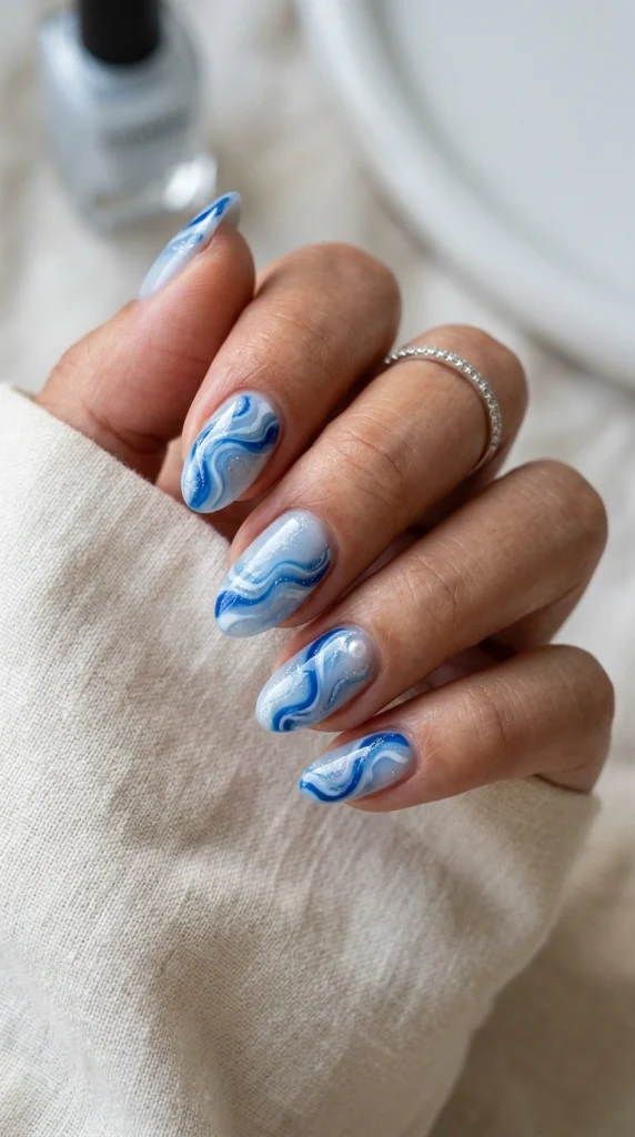 Close-up of blue and white ocean wave nail art on almond nails.