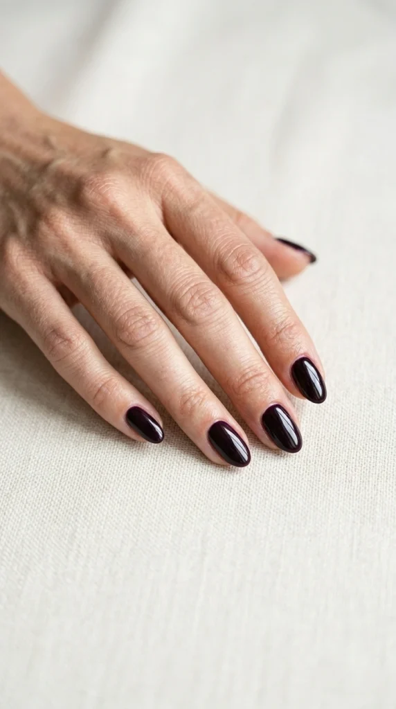 Close-up of glossy plum noir almond nails, a deep blackened plum unexpected summer nail color for 2026.