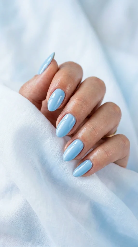 Close-up of glossy sky blue almond nails, a fresh and airy summer nail color for 2026.