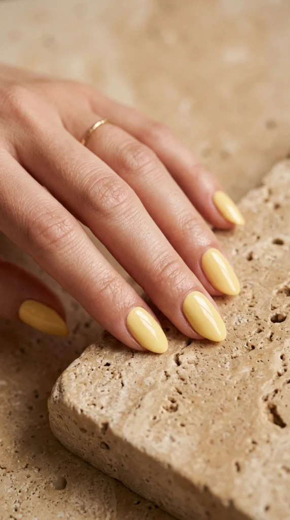 Close-up of glossy solid butter yellow almond nails in a clean minimalist summer manicure.