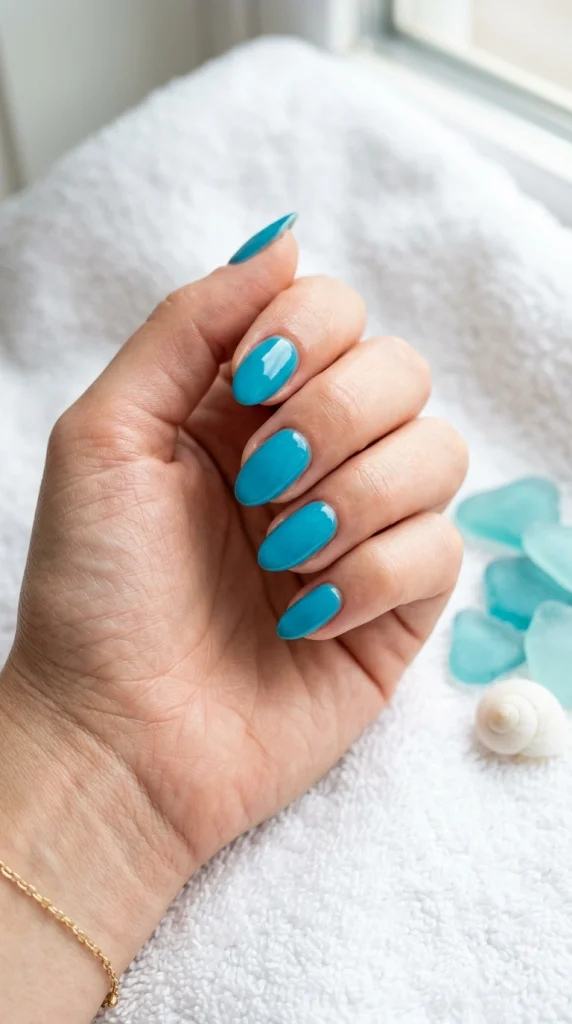 Close-up of glossy turquoise blue almond nails, a bold tropical summer nail color for 2026.