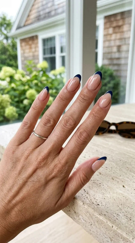 Glossy nude almond nails with navy French tips in a Hamptons-inspired quiet luxury summer setting.
