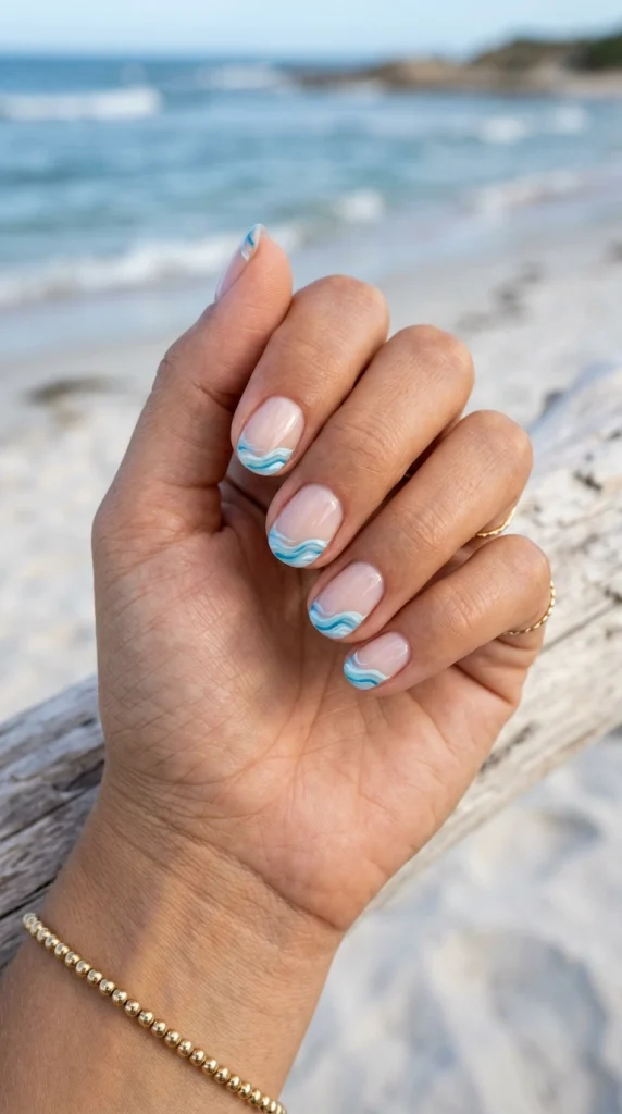 Short rounded nails with subtle blue ocean wave accents on a glossy nude base.