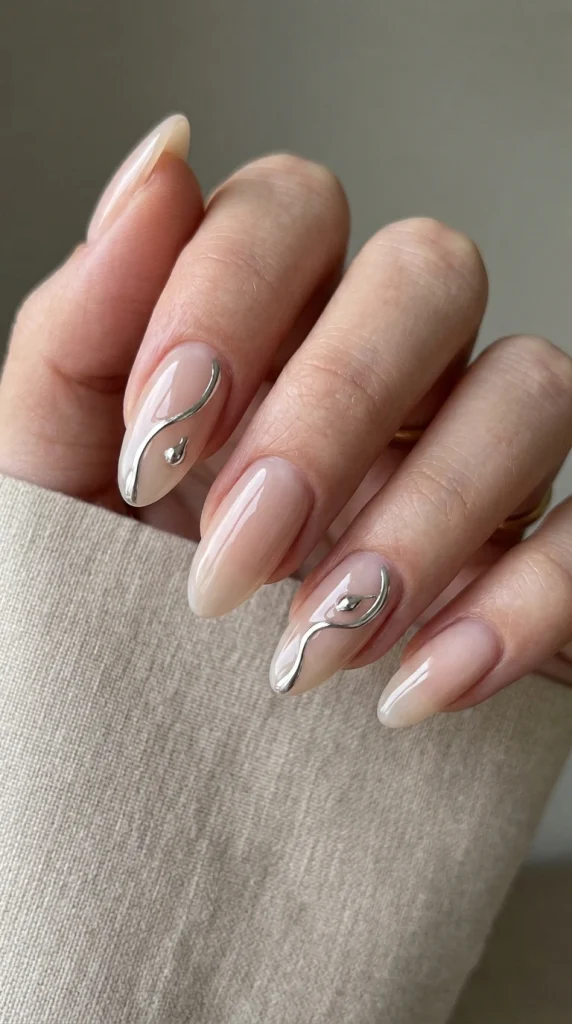 Milky nude almond nails with flowing molten silver chrome accents in a modern luxury coastal setting.
