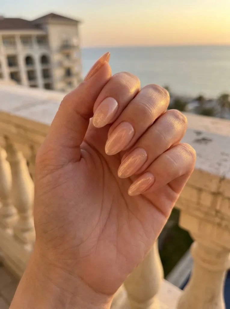 Golden Peach Shimmer manicure with a sheer peach nude base and delicate champagne gold shimmer on medium almond-shaped nails for an elegant July summer manicure.