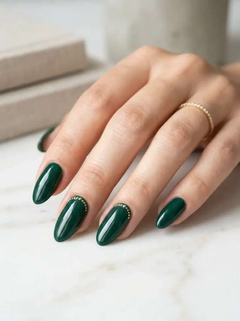20 Chic September Nail Designs for 2026 That Capture Fall’s First Glow 15 Deep emerald green almond nails with delicate gold micro-dot accents along the cuticles on a white marble surface.
