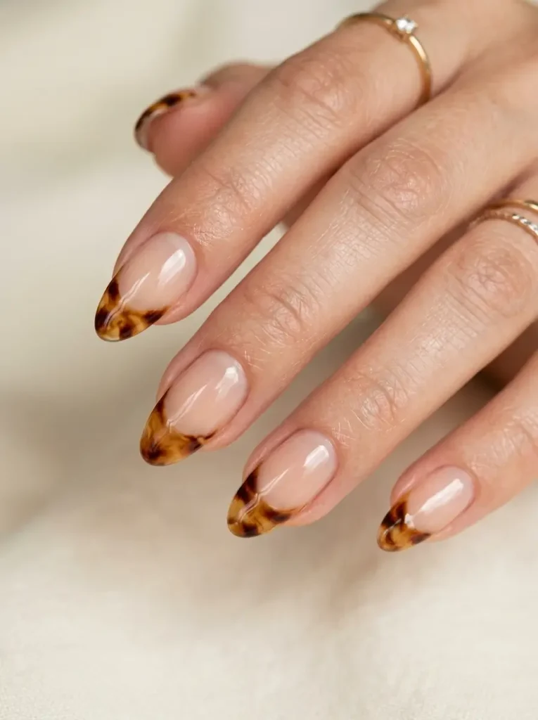 Almond nails with sheer nude bases and glossy tortoiseshell French tips in caramel, amber, and chocolate brown.