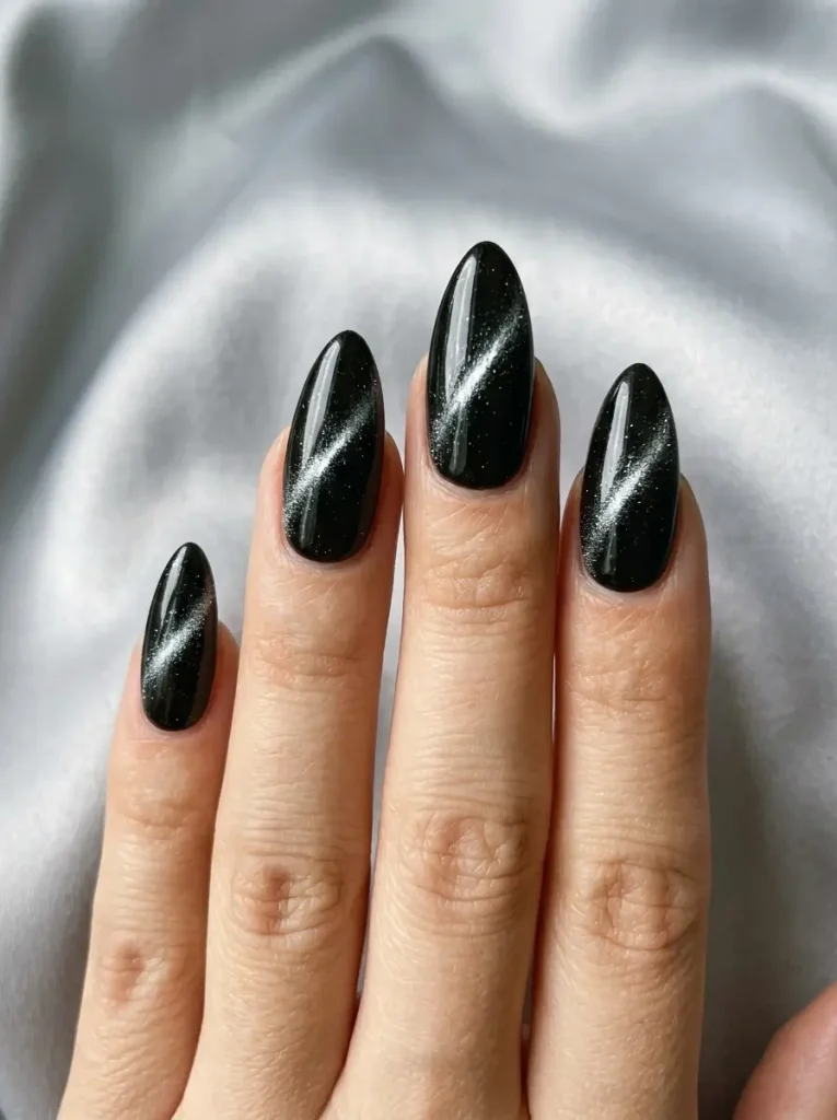 Black magnetic cat-eye almond nails with a diagonal silver light band, on a light skin tone