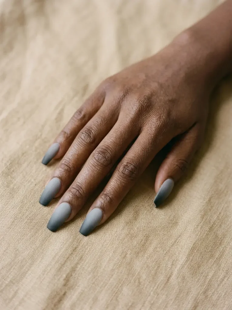 Coffin nails in a matte gray to charcoal ombré fade, on a deep skin tone