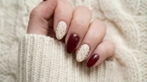 Deep burgundy sweater nails with raised cream cable knit detail, against a chunky cream wool sweater