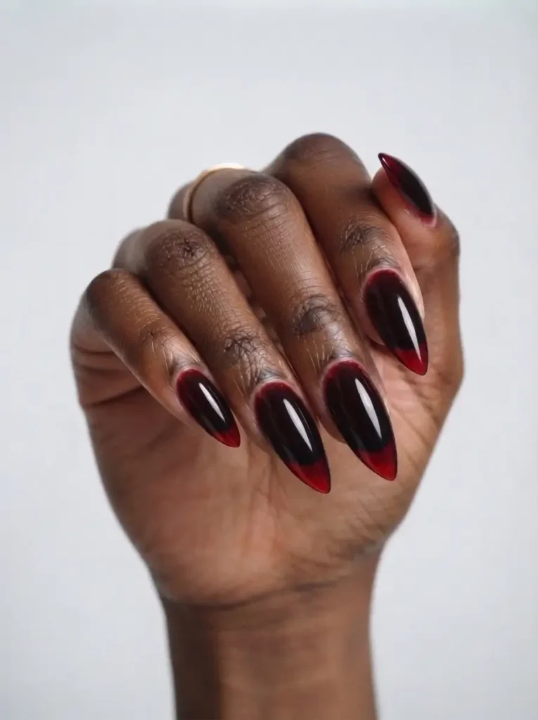 Long stiletto vampire nails in a glossy jelly black-cherry red layered over black, on a deep skin tone