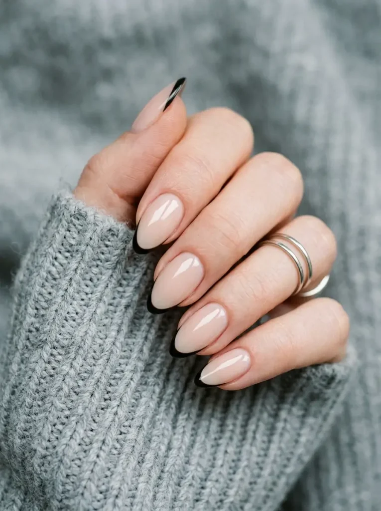 Medium almond nails with a milky nude base and a hairline black French tip, on a fair skin tone