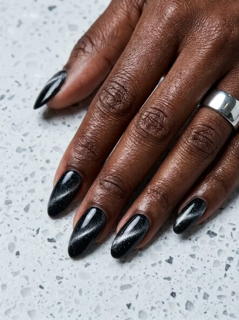 Long almond black cat eye nails with a sharp diagonal silver light band on every nail, on a deep skin tone