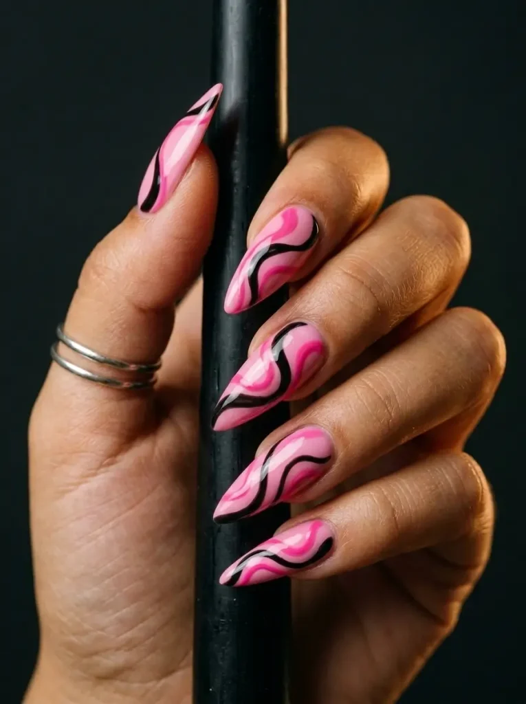 15 Pink Halloween Nail Designs for 2026, From Cute to Spooky 7 Stiletto nails in bubblegum pink with loose black and hot pink swirl lines across every nail, on an olive skin tone