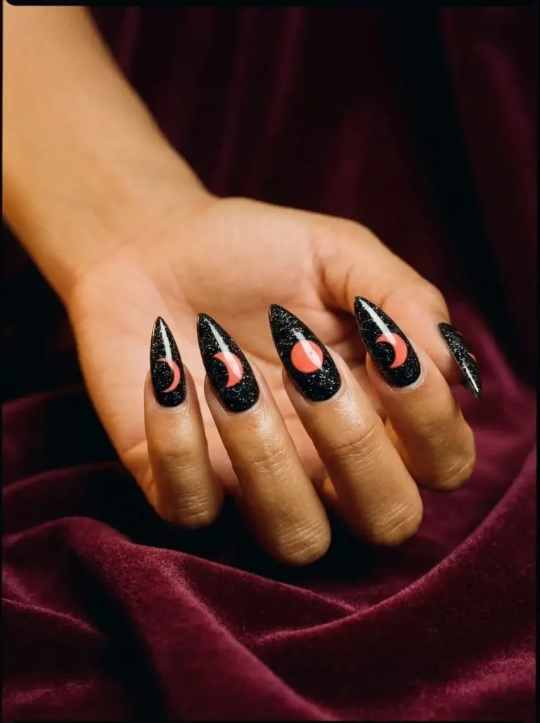 Black stiletto nails with coral-red moon phases from crescent to full moon and fine glitter, on a medium skin tone