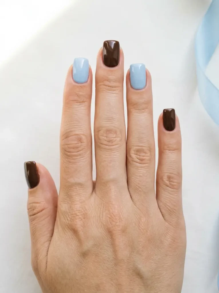 Short square nails alternating chocolate brown and powder baby blue, on a light skin tone