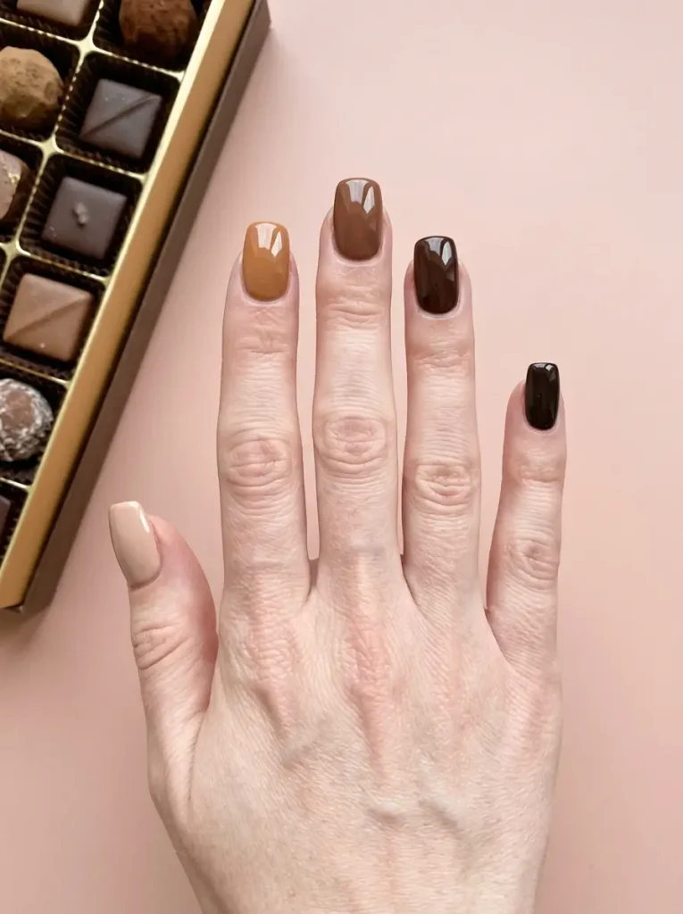 Squoval nails painted in five browns from latte to espresso, one shade per nail, on a fair skin tone