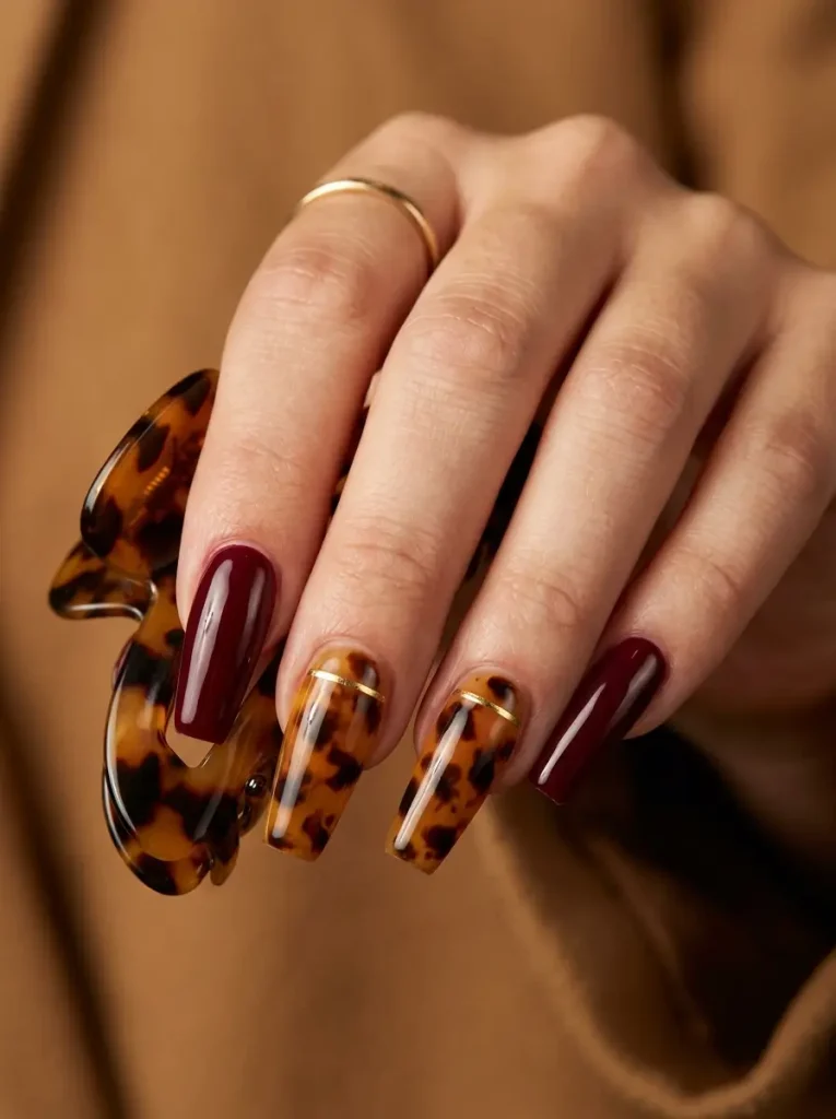 28 Fall Nail Designs for 2026, From Simple to Classy 18 Long coffin glossy burgundy nails with tortoiseshell and a thin gold base line on exactly two nails, on a fair skin tone