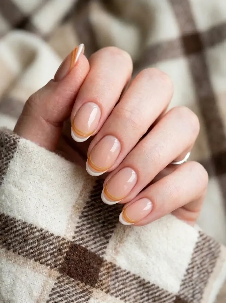 Oval nails with a thin white tip and fine floating orange and yellow lines on a sheer nude base, on a fair skin tone