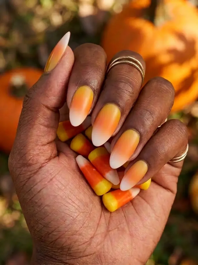 Almond nails in a candy corn ombré from yellow at the cuticle through orange to a white tip, on a deep skin tone