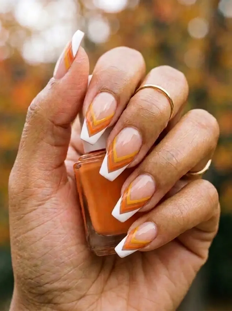 Coffin nails with a V-shaped candy corn French tip in yellow, orange and white on a sheer nude base, on a medium skin tone