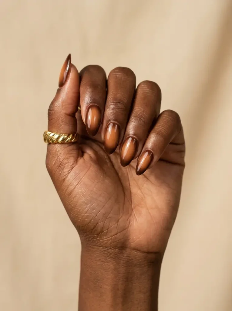 Medium almond nails with a blurred caramel aura glowing into a chocolate brown edge, on a deep skin tone