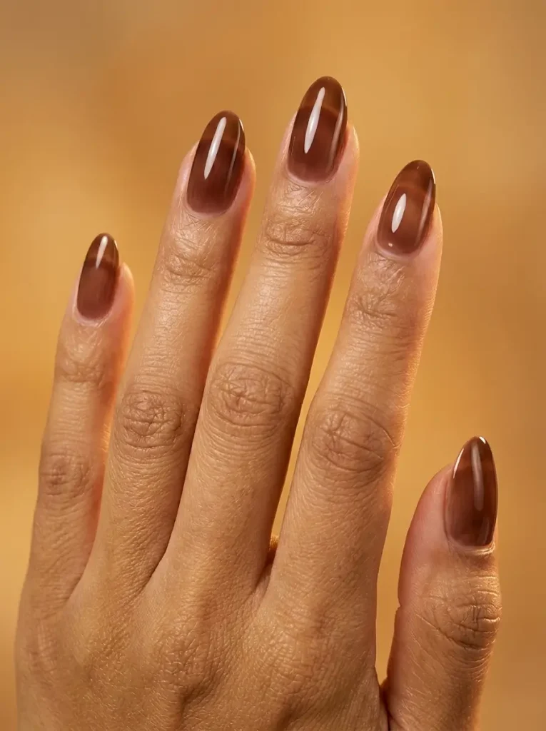 Medium almond nails in translucent chocolate brown jelly polish, glossy like brown glass, on a medium skin tone