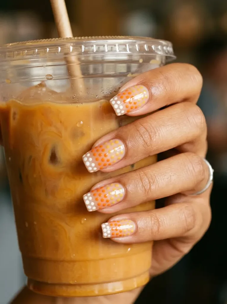 Squoval nails with yellow, orange and white dots graded from cuticle to tip on a sheer nude base, on a medium skin tone
