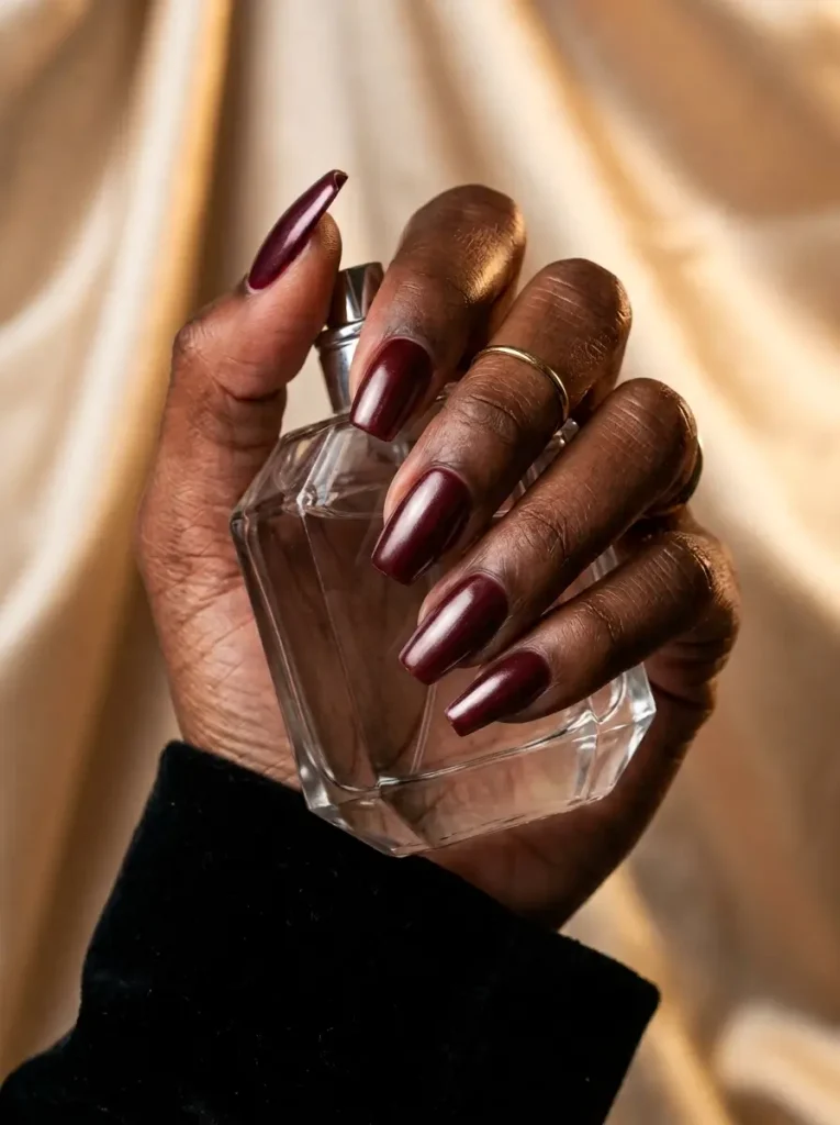 Medium coffin nails in burgundy with a glazed pearl chrome sheen, on a deep skin tone
