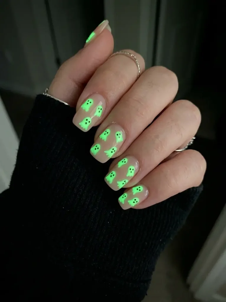Square nails in sheer nude with small glowing green glow-in-the-dark ghosts on every nail, on a light skin tone