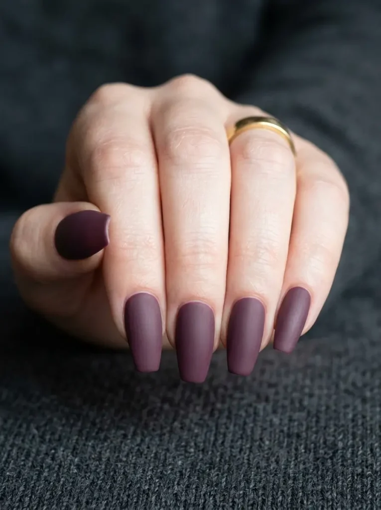 Medium coffin nails in matte dark mauve, a deep plum-leaning shade, on a fair skin tone