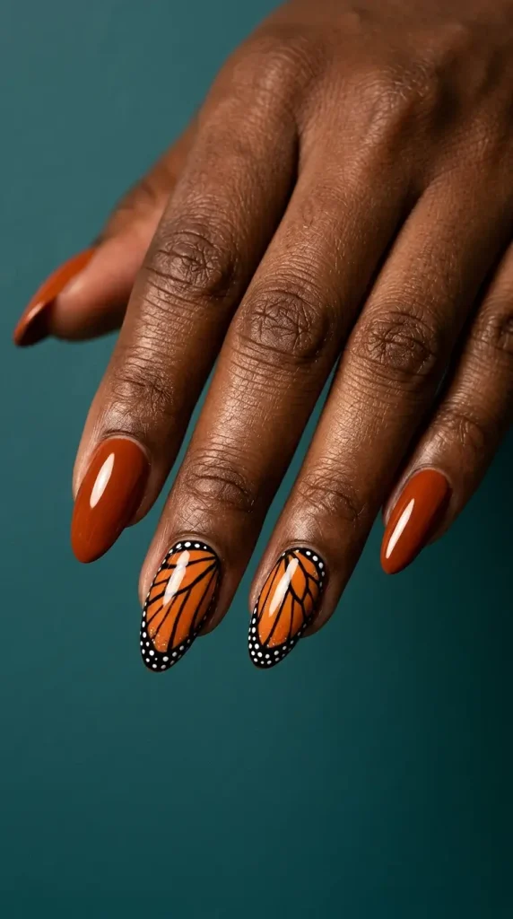 Medium almond burnt orange nails with two monarch butterfly wing accent nails in black veins, orange cells and white dots