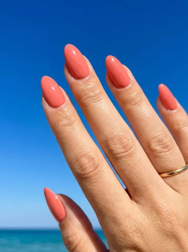 Almond nails in glossy coral on a light skin tone